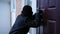 Man in balaclava breaking in house picking the lock outdoors. Young Caucasian male thief opening locked property robbing