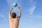 A man with a ball against a blue sky plays beach volleyball. The view from the back. Life style