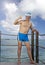 Man in a bathing suit and New Year Santa Klaus cap shows a thumb on sea background