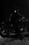 Man with beard, biker in leather jacket lean on motor bike in darkness, black background. Macho, brutal biker in leather