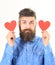 Man with beard with calm face hold red paper hearts