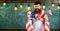 Man with beard on cheerful face holds flag of USA and clock, chalkboard on background, copy space. American educational