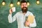 Man with beard on happy face in classroom.Teacher in eyeglasses holds book and mug of coffee or tea. Coffee break