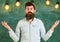 Man with beard and mustache on confused face stand in front of chalkboard. Bearded hipster in shirt, chalkboard on