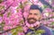 Man with beard and mustache on happy face near pink flowers. Blooming concept. Bearded man with fresh haircut with bloom