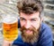 Man with beard and mustache holds glass with beer while sits on stone stairs. Friday relax concept. Hipster on cheerful