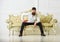 Man with beard and mustache spends leisure with book. Lecturer sit on sofa and holds book, white wall background