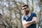 Man with beard and mustache on strict face, trees on background, defocused. Bearded man wears sunglasses on sunny day