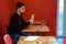 A man with a beard sits in a fast food restaurant and holds a shawarma in his hand and has a glass of coffee.