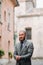 A man with a beard in a strict grey three-piece suit with a tie in the old town of Sirmione, a Stylish man in a grey suit in Italy