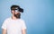 Man with beard in VR glasses, light blue background. Digital technology concept. Hipster on serious face enjoy virtual