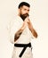 Man with beard in white kimono on white background. Taekwondo master with black belt practices attack or defense