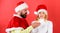 Man with beard and woman in santa hat on red background. Girl disgusted face celebrate christmas. Couple celebrate