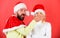 Man with beard and woman in santa hat on red background. Man covers mouth of girl to keep secret. Couple celebrate