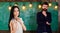 Man with beard and young lady teacher stand in classroom, chalkboard on background. Lady teacher and bearded hipster