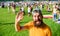 Man bearded hipster in front of crowd people green field background. Hipster in cap visiting social event picnic fest or