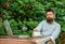Man bearded hipster make pause for drink coffee and think while sit with laptop. Guy drinks coffee relaxing terrace