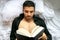 Man in bed with open shirt and pecs reading hardback book