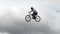 Man on bicycle jumps high in slow motion, cloudy background