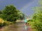 Man on bicycle rides under the rain, going through puddles toward the rainbow. Water evaporates on hot ground and thick steam han