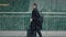 Man in black coat with suitcase walking on background of glass windows