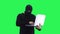 A man in a black mask enters data into a laptop, on a green screen background