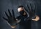 Man in a black mask and medical gloves shows STOP with his hands, on a dark background. The concept of fear and protection against