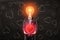 Man in black suit with light bulb instead head, levitating red glaring heart with his palms, standing against black