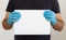 A man in a black t-shirt and medical gloves holds a white sheet of paper. Mockup. Coronavirus. Quarantine. Warning