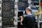 A man in a black T-shirt is near the main router. System administrator with a laptop sitting in the server room. Programmer checks