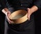 Man in black uniform holding empty vintage round wooden sieve for sifting flour