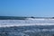 A man in a black wet suit surfing on the gorgeous vast deep blue ocean water with waves breaking into the shore