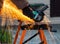 A man in the black working gloves cuts metal using an angle grinder tool with beautiful yellow sparks on a work bench