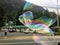 A man blowing huge bubbles along the side of the road, trying to sell bubble makers to people passing by