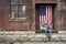 Man in blue jeans with acoustic guitar and american flag on old brick factory loading dock