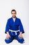 A man in a blue kimono with a white sash sits on the floor. A beginner fighter of oriental martial