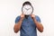 Man in blue shirt hiding face behind wall clock display, wasting his time, procrastination, organization of working time