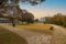 A man in a blue shirt jogging on a footpath in a park with a stunning autumn landscape surrounded by gorgeous autumn colored trees