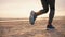 Man in blue sneakers running along sand beach at sunset