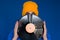 man in a blue sport 90s style jacket and yellow hat holding vinyl record, man hides his face under vinyl disc