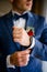 Man in blue suit adjusts white sleeve over watch