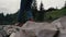 Man in boots hiking on rocks at river. Male hiker walking in summer mountains