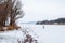 Man is boring a hole for fishing on a snowy frozen river in the distance. Winter landscape