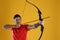 Man with bow and arrow practicing archery on yellow background