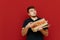 Man with a box of pizza stands on a red background, takes a slice of fast food and looks away with a serious face. Hungry bearded