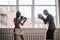 A man with boxing paws on his hands teaches the technique of hitting a novice girl in a light gym