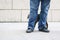 Man or boy standing on outdoors white tile with marble block wall behind in blue jeans with cat rubbing up against his legs -