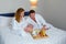 Man brought breakfast tray to hotel room and placed it on bed next to woman.