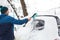 A man brushes snow from a car after a snowfall. A hand in a blue jacket with a car broom on the white body. Winter weather