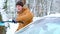 A man brushes snow from a car after a snowfall. A hand in a mustard jacket with a car broom on the white body. Winter weather cond